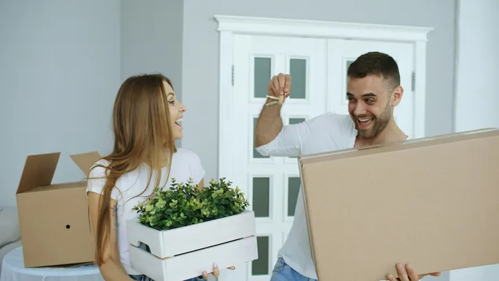 A couple laughing as they unpack in their new home, holding up the keys
